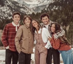 a group of people standing next to each other in front of snow covered mountains and trees