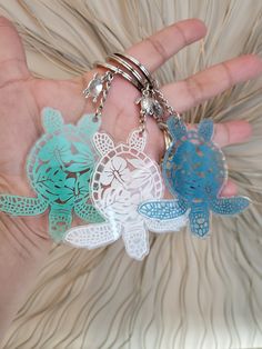 the hand is holding three key chains with sea turtles on them, one in blue and one in white