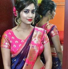 a woman in a pink and blue saree is looking at herself in the mirror