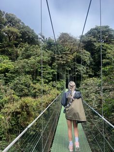 a woman walking across a suspension bridge in the forest