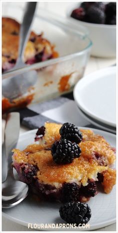 a slice of blackberry cobbler on a plate with a fork and bowl in the background