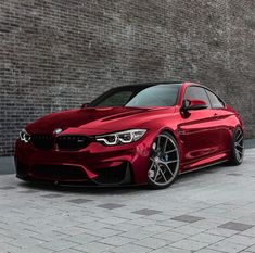 a red bmw is parked in front of a brick wall with black rims on it