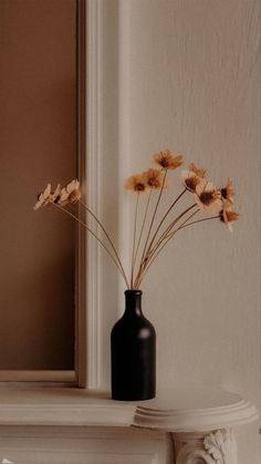 a black vase filled with dried flowers on top of a mantle