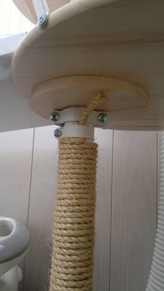 a white toilet sitting next to a wooden pole with rope hanging from it's sides