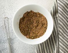 a white bowl filled with spices on top of a table next to two spoons