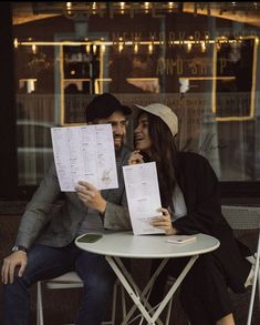 a man and woman sitting at a table with some papers in front of them smiling