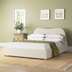 a white bed sitting on top of a wooden floor next to a green painted wall