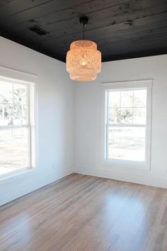 an empty room with two windows and a light fixture hanging from the ceiling above it