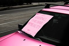 a pink car parked on the side of the road with a sign attached to it