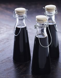 three small bottles are sitting on a wooden table, one is filled with black liquid and the other has a white cap