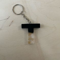 a cross shaped keychain is hanging on a white surface with a black piece of wood sticking out of it