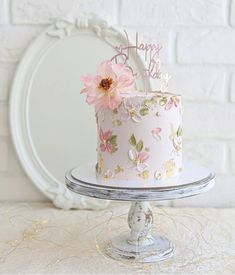 a pink and gold birthday cake with flowers on it sitting on top of a table