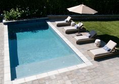 an empty pool with lounge chairs and umbrellas next to the side walk in front of it