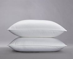 two white pillows stacked on top of each other in front of a gray background,