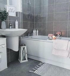 a bathroom with grey tiles and white fixtures, including a sink, bathtub, toilet and rug