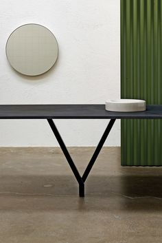 a black table sitting in front of a green wall with a white bowl on it