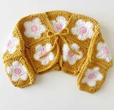 a crocheted yellow jacket with white and pink flowers on the front, tied in a knot