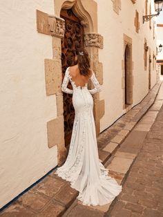 a woman in a wedding dress leaning against a wall with her back to the camera