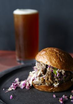 a pulled pork sandwich with cole slaw on a black plate next to a glass of beer