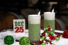 two green candles sitting on top of a table covered in snow next to christmas decorations