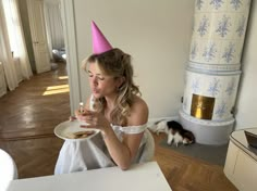 a woman sitting at a table with a plate of food in front of her, wearing a pink party hat