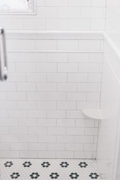 a white tiled bathroom with black and white floor tiles on the shower wall, along with a toilet paper dispenser