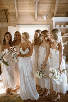 a group of women standing next to each other in white dresses holding bouquets and flowers