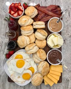 an assortment of breakfast foods laid out on a cutting board with eggs, biscuits and fruit