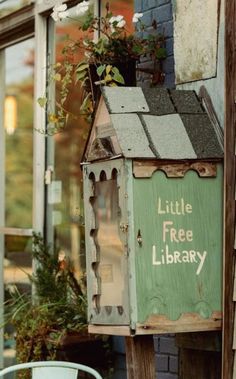 a little free library sign on the side of a building with potted plants in it