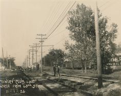 an old black and white photo of two men standing on train tracks near power lines