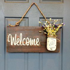 a mason jar with flowers hanging from it's side on a welcome sign attached to a door