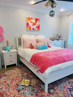 a white bed with pink and blue pillows on top of it next to a colorful rug