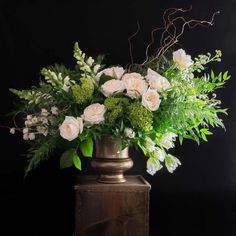 a vase filled with white and green flowers on top of a wooden table next to a black wall