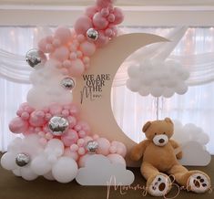 a teddy bear sitting next to a balloon arch with the moon and clouds on it