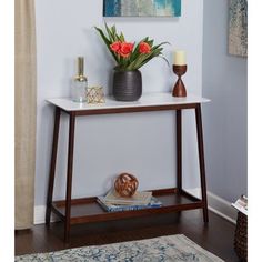 a vase with flowers on top of a white table next to a lamp and rug