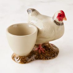 a ceramic chicken sitting on top of a cup next to it's saucer