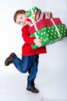 a young boy carrying a large green and red wrapped present