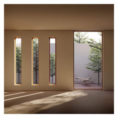 an empty room with three windows and a table in the middle, near some trees