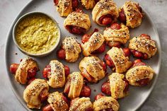 hot dogs wrapped in bread and topped with mustard on a plate next to a dipping sauce