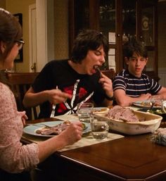 a group of people sitting around a table with food in front of them and eating