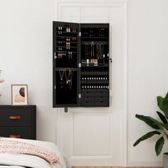 a black jewelry cabinet sitting on top of a bed next to a potted plant