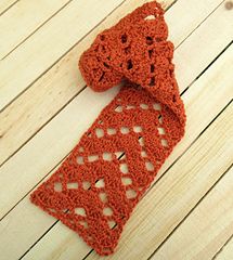 an orange crocheted scarf sitting on top of a wooden floor