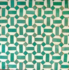 a green and white tiled wall with small squares in the center, on top of a red tile floor