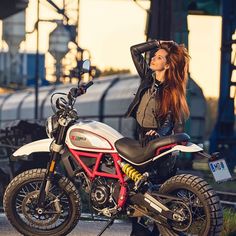 a woman sitting on top of a motorcycle next to a train track with her hair blowing in the wind