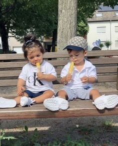 two young children sitting on a bench eating ice cream and popsicles in front of them