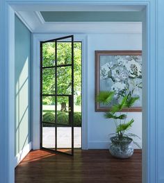 an open door leading into a room with a potted plant on the floor and a painting hanging above it