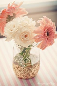 some flowers are in a glass jar on a table with sand and shells around it