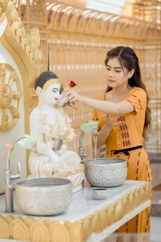 a woman is decorating a statue with a flower in front of a bowl on a table