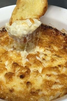 a piece of bread is being dipped with melted cheese on top of a dish filled with macaroni and cheese