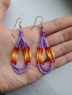 Purple and fire colored beaded dangle earrings How To Make Beaded Dangle Earrings, Orange And Purple Jewerly Beads, Purple Dangle Earrings With Tiny Beads, Rainbow Dangle Earrings With Tiny Beads, Purple Beaded Earrings With Colorful Beads, Purple Beaded Dangle Earrings With Tiny Beads, Orange Beaded Dangle Jewelry, Orange Dangle Jewelry With Colorful Beads, Colorful Dangle Beaded Earrings